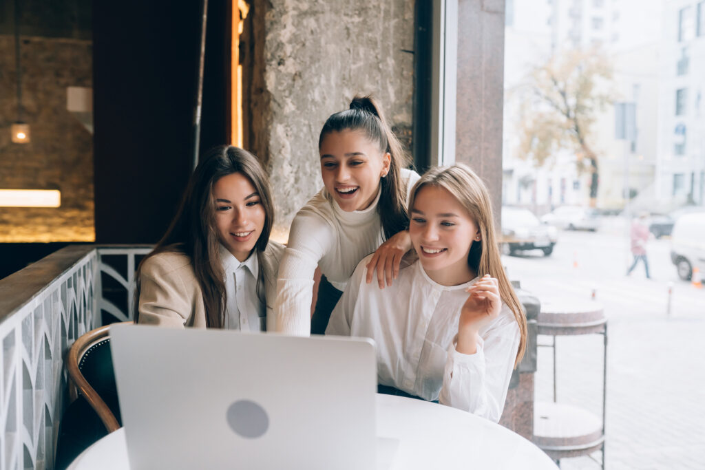 A group of gen z women in a cafe are looking at a laptop